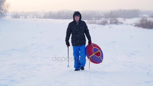 Ο τύπος ανεβαίνει στο χιονισμένο λόφο με snowtube.slow κίνηση. χιόνι χειμερινό τοπίο. Ηλιοβασίλεμα ώρα — Αρχείο Βίντεο