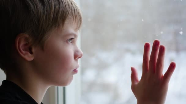 Ребенок сидит на подоконнике и смотрит в окно на снег крупным планом — стоковое видео