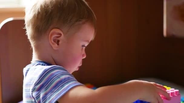 Un niño pequeño juega en el constructor. Juego de los niños diseñador. Cubos de colores . — Vídeos de Stock