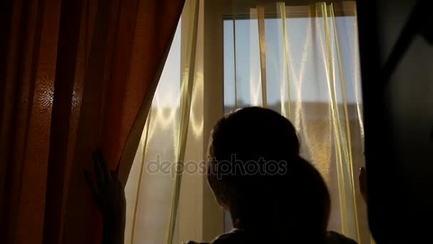 The girl opens the curtains and played with his hands through the suns rays. silhouette of a girl — Stock Video