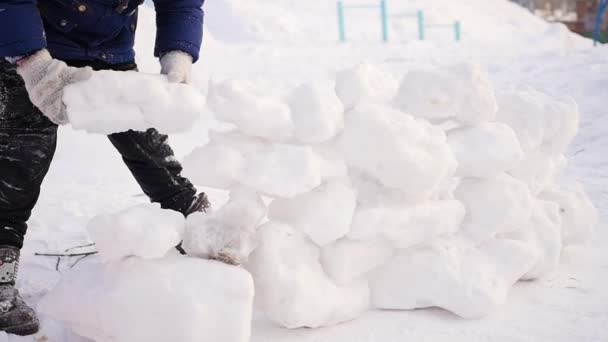 Child playing outdoors in winter. The child builds a wall of snow stones — Stock Video