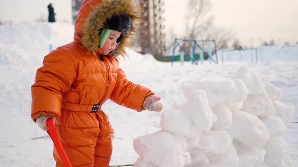 Dítě hrát venku v zimě. Dítě staví zeď sníh kamenů — Stock video