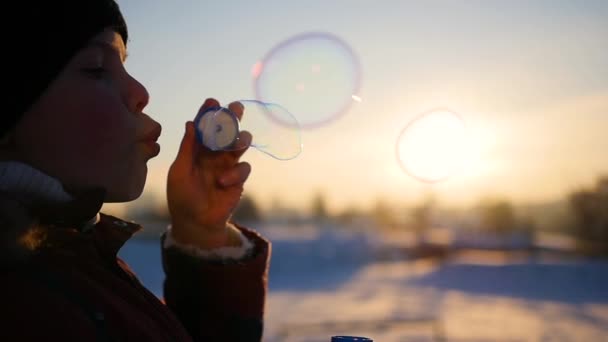 Fiú szappanbuborékok fúj a parkban, örömében a téli naplemente — Stock videók