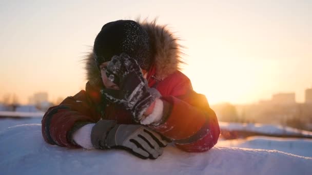 Ένα παιδί κύματα το χέρι στο χειμερινό πάρκο, με φόντο το ηλιοβασίλεμα. χιόνι χειμερινό τοπίο. Ηλιοβασίλεμα ώρα — Αρχείο Βίντεο