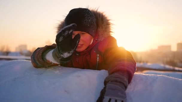 Ребенок машет рукой в зимнем парке, на фоне заката. снежный зимний пейзаж. Время заката — стоковое видео