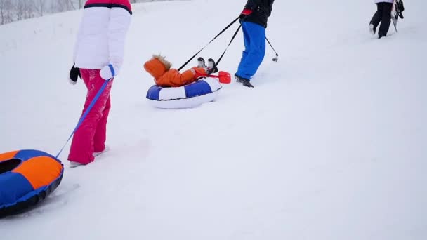 La familia se eleva a la colina nevada con tubo de nieve. cámara lenta. nieve invierno paisaje. Descanso activo, deportes — Vídeos de Stock