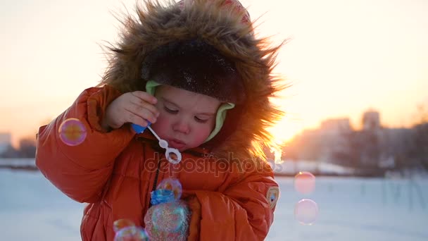 Boy blows soap bubbles in the Park with delight at winter sunset — Stock Video