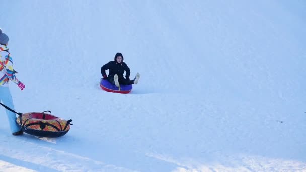 Novosibirsk, Rusko - 27. prosince 2016: Šťastný chlap jízdy a usmívala se na snowtube na zasněženém kopci a pádu — Stock video