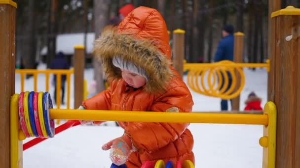 Boldog gyermeke kipróbálhassa a szórakoztató játék a parkban, egy napsütéses téli napon. Havas téli táj. a szabadban — Stock videók