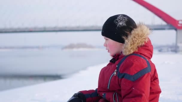 Het kind zit op de oever en kijken in de verte. Winterlandschap — Stockvideo