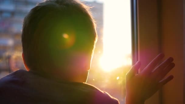 Хлопець дивиться у вікно на сонце. Грає руку з сонячним світлом — стокове відео