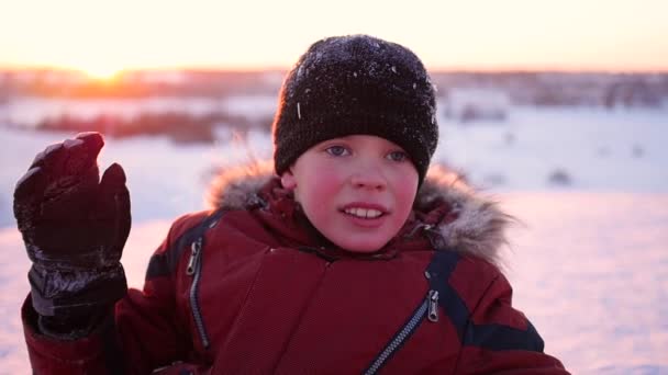 Un niño agita la mano en el parque de invierno, en el fondo de la puesta del sol — Vídeos de Stock