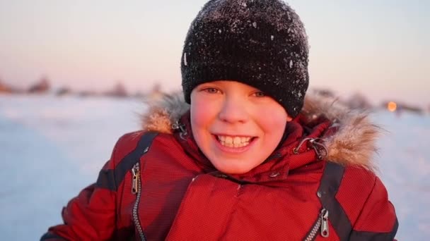 Ένα χαμόγελο παιδιού στο χειμερινό πάρκο, με φόντο το ηλιοβασίλεμα — Αρχείο Βίντεο