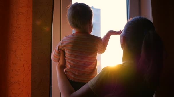 Dívka si hraje s dítětem poblíž okna. Čas západu slunce. Sluneční světlo — Stock video