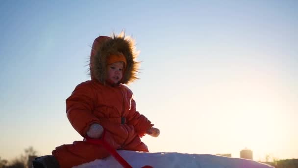 Kind spelen op een besneeuwde heuvel. Winterlandschap. Zonsondergang tijd — Stockvideo