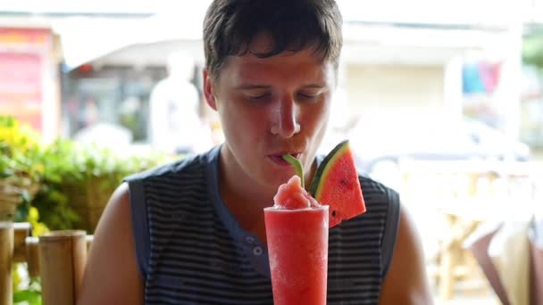 Хлопець п'є кавуновий коктейль у вуличному кафе — стокове відео