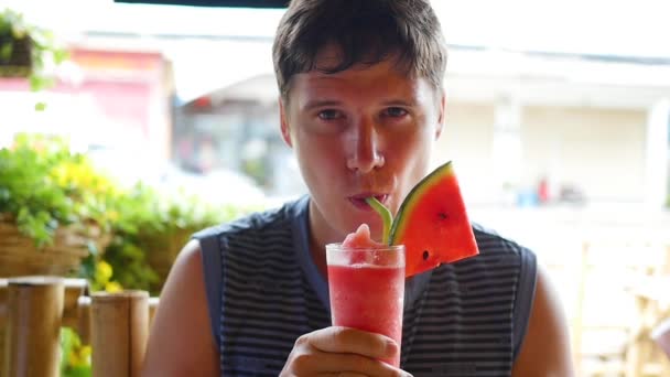 Der Kerl trinkt einen Wassermelonencocktail in einem Straßencafé — Stockvideo