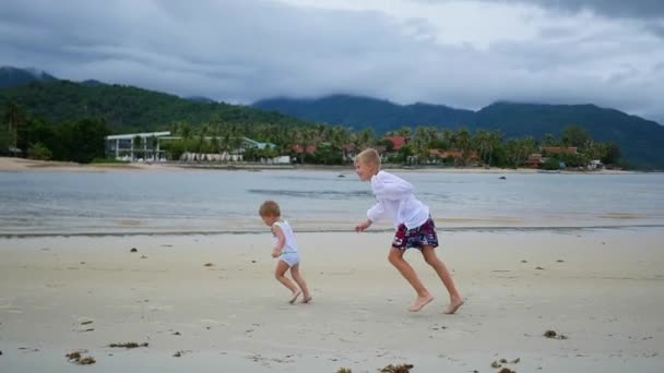 Die Kinder laufen fröhlich am Strand entlang und erzeugen einen Wasserstrahl — Stockvideo