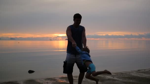 Guy cirkelen baby bedrijf handen op strand bij zonsondergang. — Stockvideo