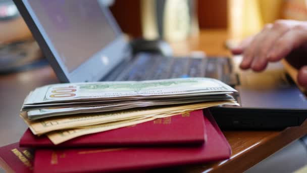 Hands typing text on laptop, close-up of money and passports — Stock Video