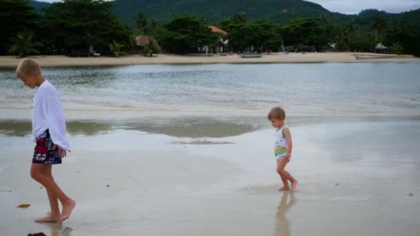 Los niños corren alegremente a lo largo de la playa, creando un chorro de agua — Vídeos de Stock