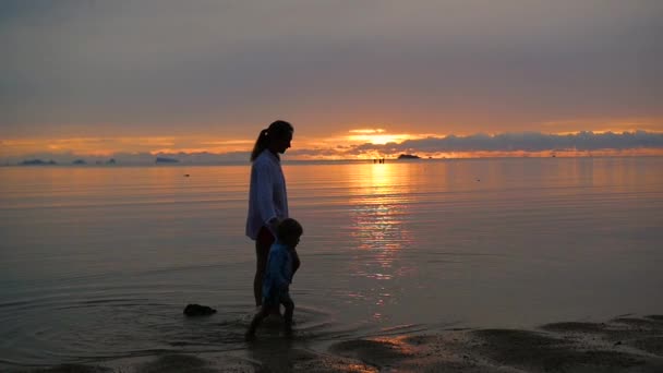 Flickan med barnet gå promenader och spela på stranden vid solnedgången tid — Stockvideo