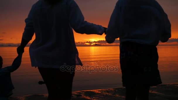 Familia cogida de la mano corriendo por la playa hacia el mar al atardecer — Vídeo de stock