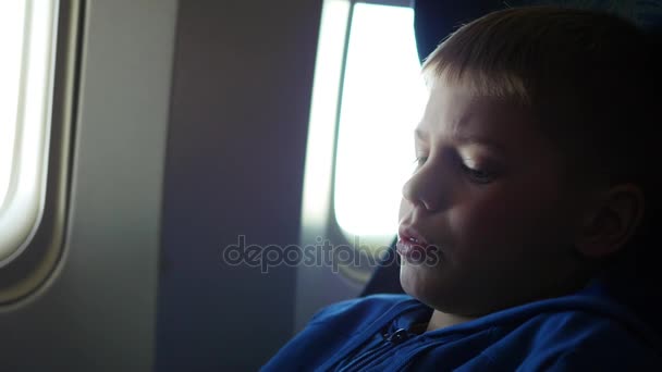 Ένα παιδί που κοιτάζει έξω από το παράθυρο ενός αεροπλάνου σε μια ηλιόλουστη ημέρα — Αρχείο Βίντεο
