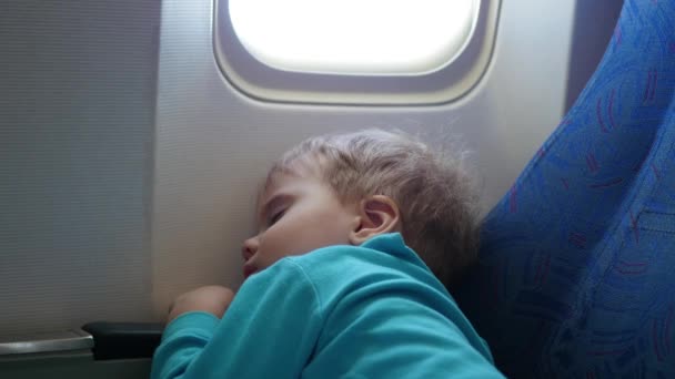 Ребенок спит в самолете на стуле рядом с окном — стоковое видео