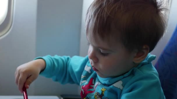 Egy gyermek ül, és felhívja a repülőgép az ablak mellett — Stock videók