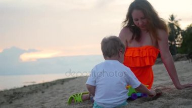 Kum ile sahilde günbatımı zaman oynayan bir çocuk kızla