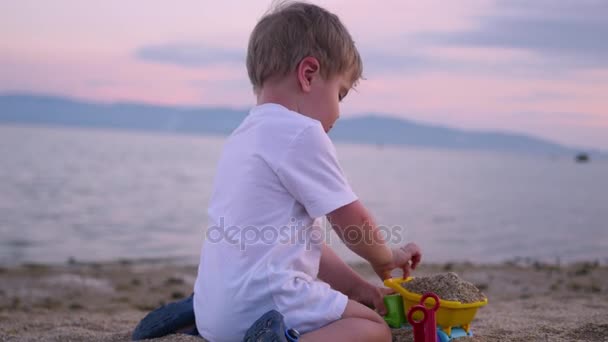 Niño jugando con arena en la playa al atardecer — Vídeos de Stock