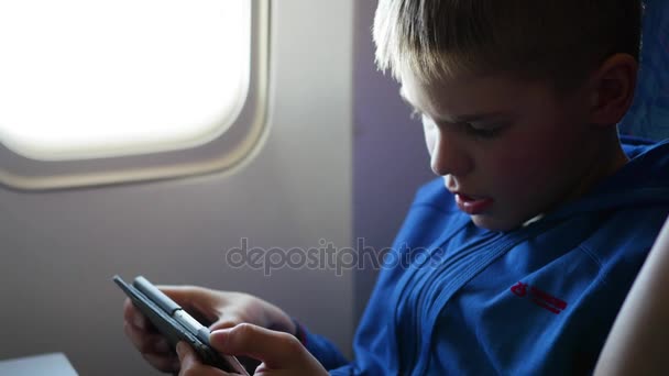 Het kind houdt de mobiele telefoon in het vliegtuig in de buurt van het venster — Stockvideo