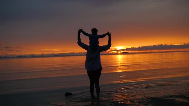 La chica con el niño ir a pasear y jugar en la playa al atardecer — Vídeo de stock