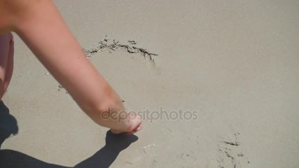 Das Mädchen macht eine Zeichnung im Sand. die Meereswelle spült an einem sonnigen Tag das Muster vom Sand weg — Stockvideo