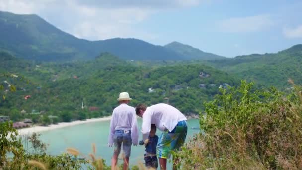 Ein junger Mann mit zwei Kindern spielt vor dem Hintergrund von Meer und Bergen — Stockvideo