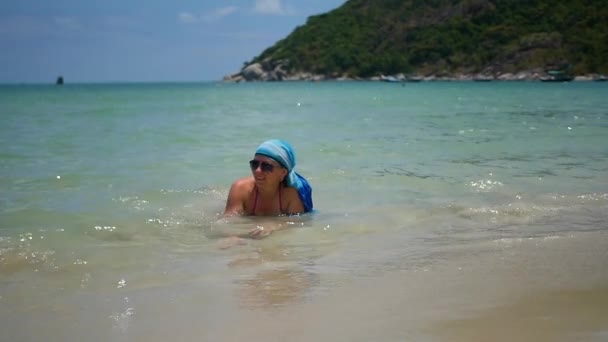 Chica tumbada en la playa y disfrutando de las olas del mar en un día soleado — Vídeo de stock