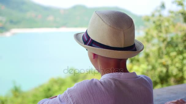 El niño en el sombrero mirando a la distancia el mar y las montañas desde el mirador. vista — Vídeos de Stock