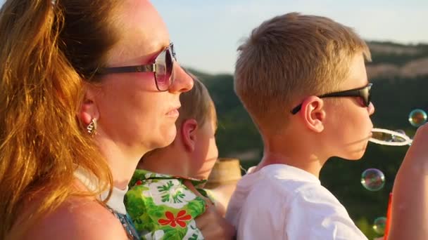 Junge macht Seifenblasen mit Mama und Bruder. Panoramablick — Stockvideo