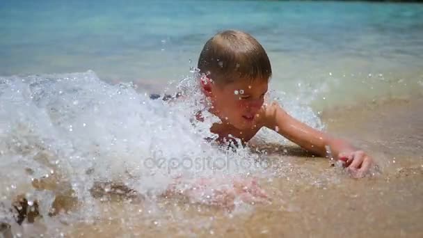Das Kind liegt am Strand und schwimmt an einem sonnigen Tag in den Wellen des Meeres — Stockvideo