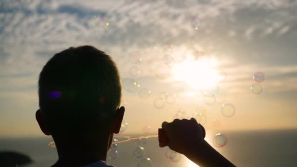 Хлопчик робить мильні бульбашки. Крупним планом. Панорамний вид. Захід сонця — стокове відео