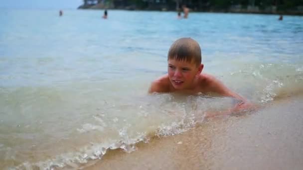 El niño se encuentra en la playa y nada en las olas del mar en un día soleado — Vídeos de Stock