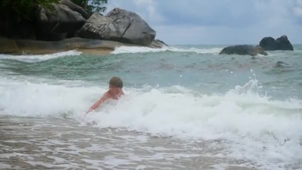 El niño se encuentra en la playa y está bañado en grandes olas marinas — Vídeos de Stock