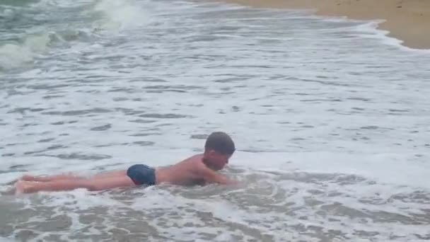 Barnet ligger på stranden och badar i stora havsvågor — Stockvideo