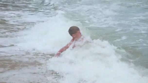 Το παιδί βρίσκεται στην παραλία και κολυμπά με τα κύματα της θάλασσας, σε μια ηλιόλουστη ημέρα — Αρχείο Βίντεο