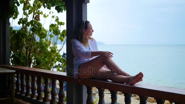 Девушка сидит на террасе и смотрит на море — стоковое видео