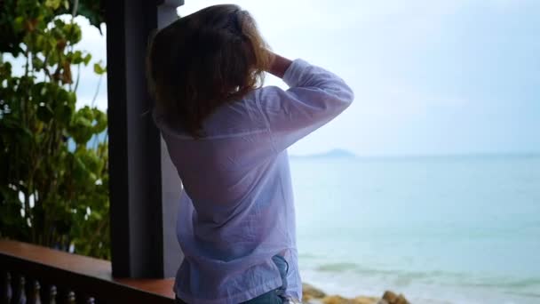 La chica está de pie en la terraza y mira hacia el mar — Vídeos de Stock