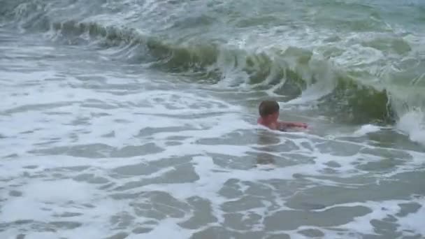 Το ευτυχισμένο παιδί βρίσκεται στην παραλία και κολυμπά με τα κύματα της θάλασσας, σε μια ηλιόλουστη ημέρα — Αρχείο Βίντεο