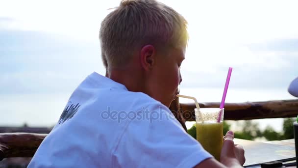 Ένας νεαρός άνδρας σε ένα καφέ, πίνοντας ένα κοκτέιλ στη βεράντα. σε εξωτερικούς χώρους — Αρχείο Βίντεο