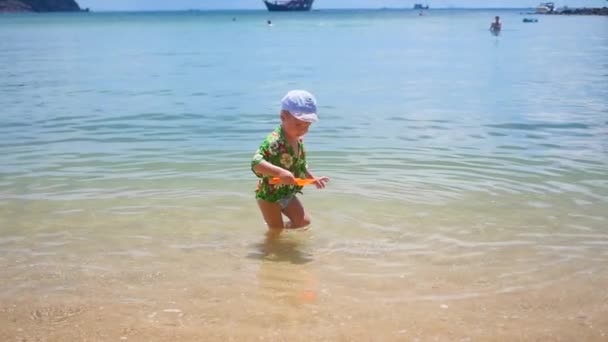 Un niño jugando en la arena de la playa en el día soleado — Vídeo de stock